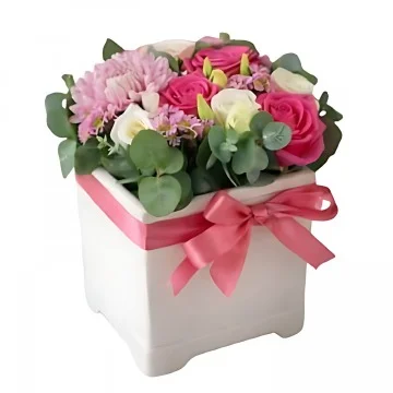 Ett lågt arrangemang till nyfödd med rosa band runt en vit kruka med rosa snittblommor och grönt.