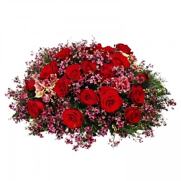 En låg begravningsdekoration med röda snittblommor och grönt.